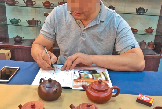 6 月20 日，宜兴中国陶都陶瓷城的一家门店内，店主拿出一把“代工壶”后，又拿出一张空白的收藏证书，模仿国家工艺美术师徐某的字迹“签售”。新京报记者 郑新洽 摄