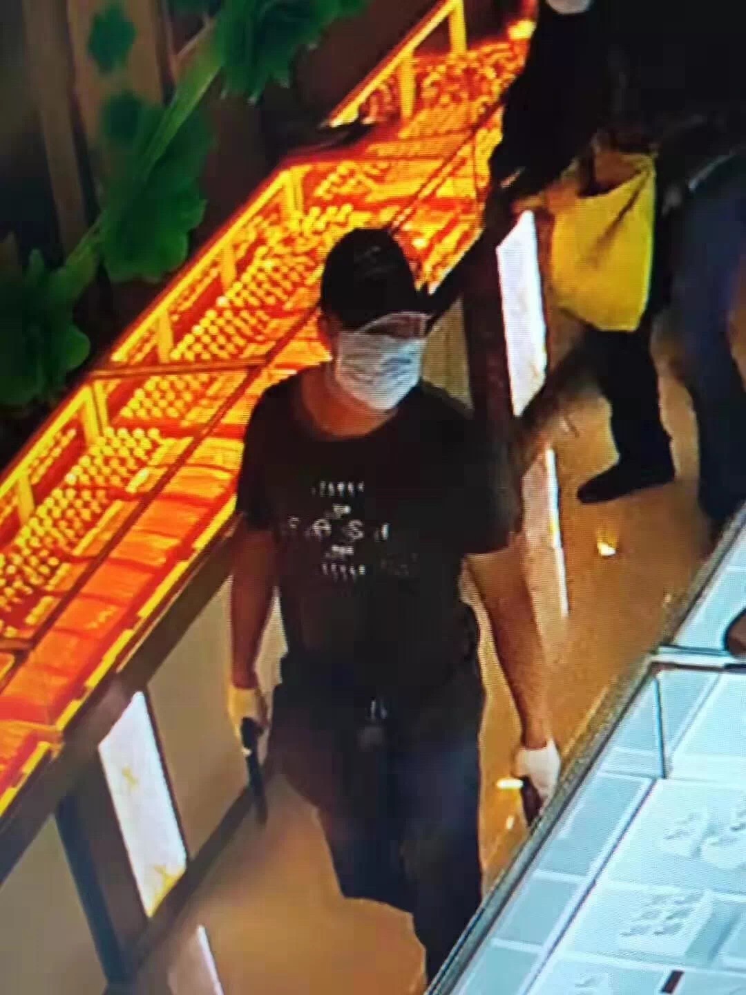一男子掩住面目走在柜台间，手中持一疑似枪支的黑色物品。受访者供图