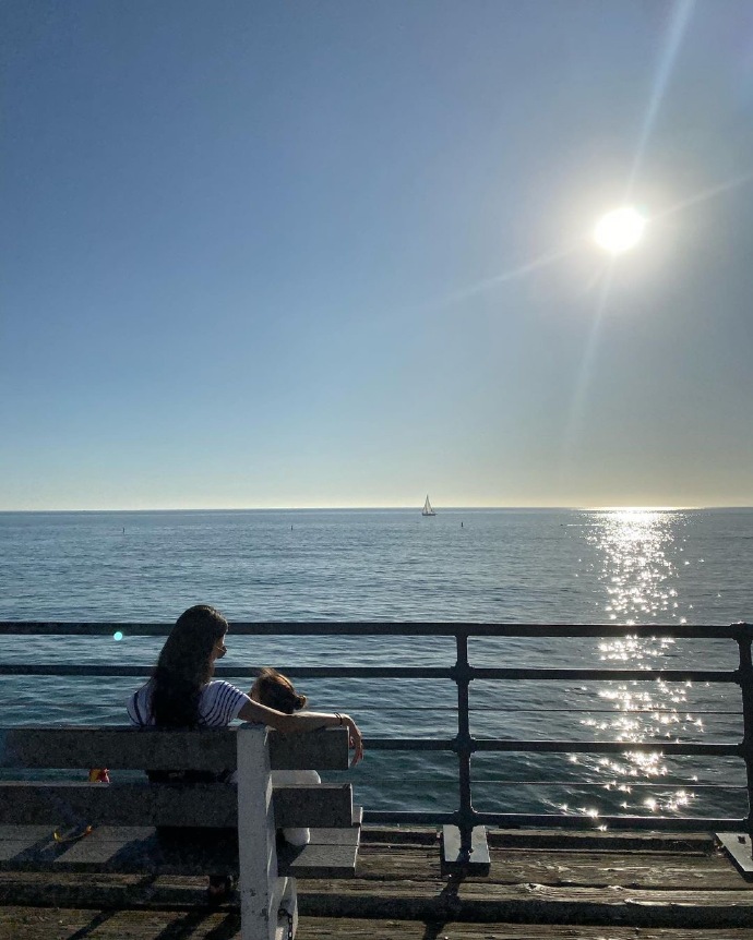 在一片海面上,太阳悬挂在天空中,阳光洒在海面上泛着金光,在海边一个