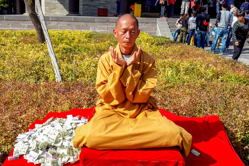 一个和尚室外打坐,一言不发,游客纷纷捐钱布施,零钱堆成小山