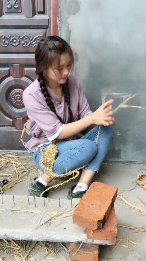 穿着一身朴素的衣服,正坐在地上用稻草编织草鞋,美女的手很灵活,一下