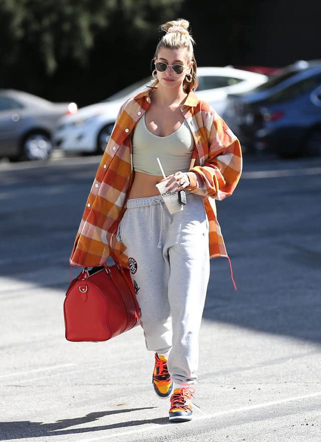 海莉·鲍德温身穿一件橘色的格纹衬衫,搭配短款运动背心以及运动裤
