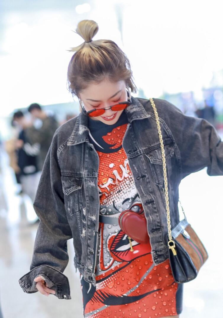 王菊扎丸子头穿牛仔夹克内搭橘色印花短裙现身机场行走间星范十足
