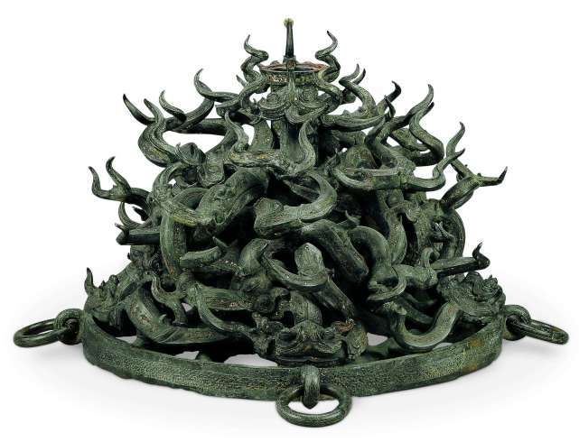 铜鼓座器造型奇特,口沿作虎首和龙盘绕一周龙独角上翘,器身满饰蟠虺纹