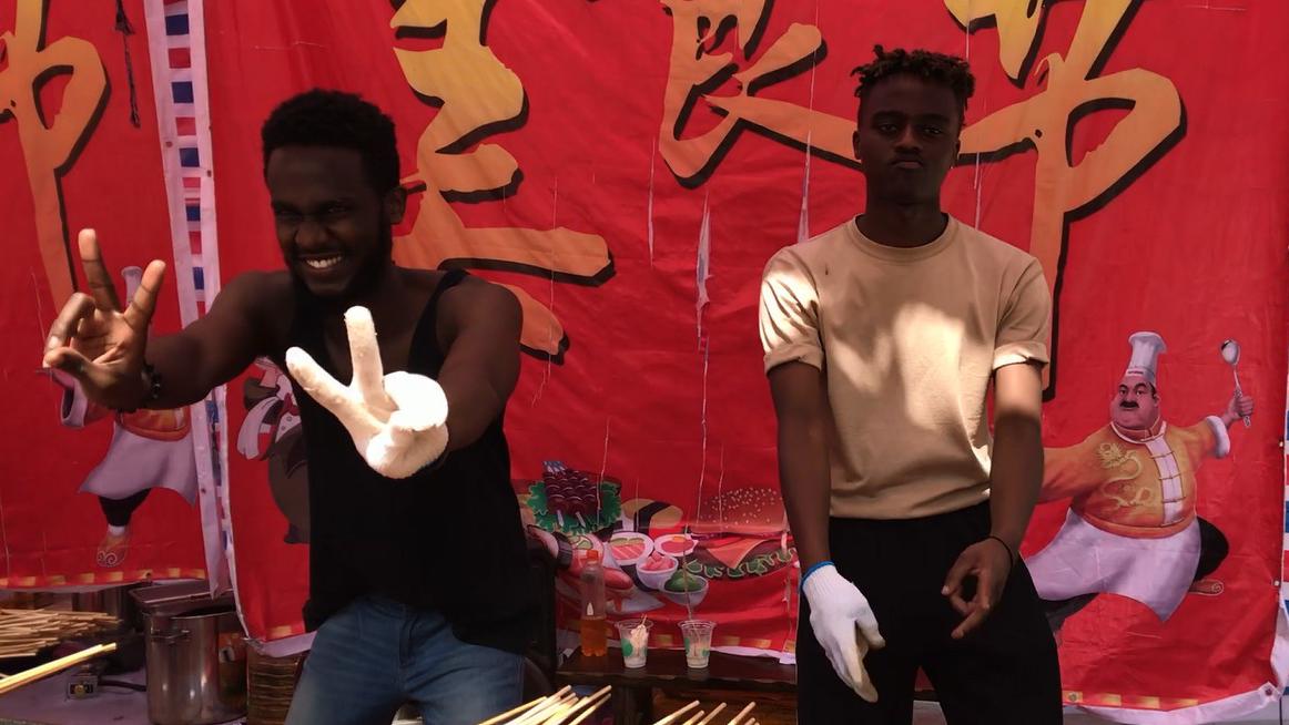 非洲黑人小伙边舞边卖羊肉串,暗背景下白手套特别显眼眼