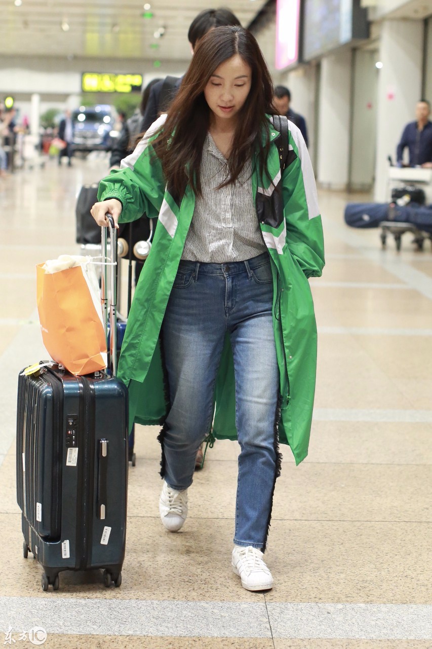 小陶虹绿色风衣搭配蓝色牛仔裤现身机场,推着拉杆行李箱面带微笑