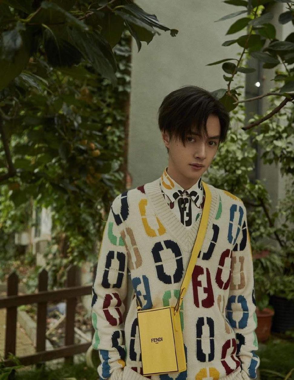 官鸿身穿v领毛衣内搭同款印花衬衫,再搭配一只黄色立方小包