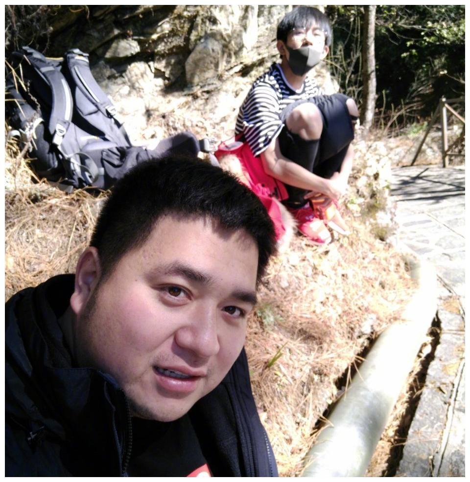 视频"中的易烊千玺假装在自拍,实际是在偷拍背后开心唱歌的助理胖虎