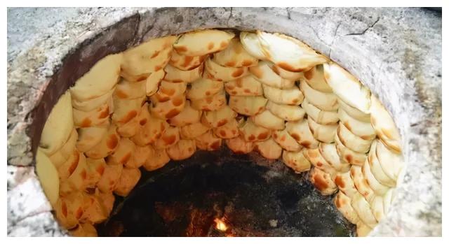 包子变得金黄焦香,此时专业制作烤包子的民族师傅手持铲子伸进馕坑,将