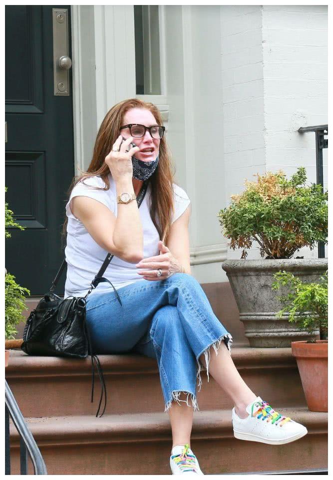 波姬·小丝没有化妆,戴着眼镜,正坐在家门口打电话,身穿白t恤和牛仔裤