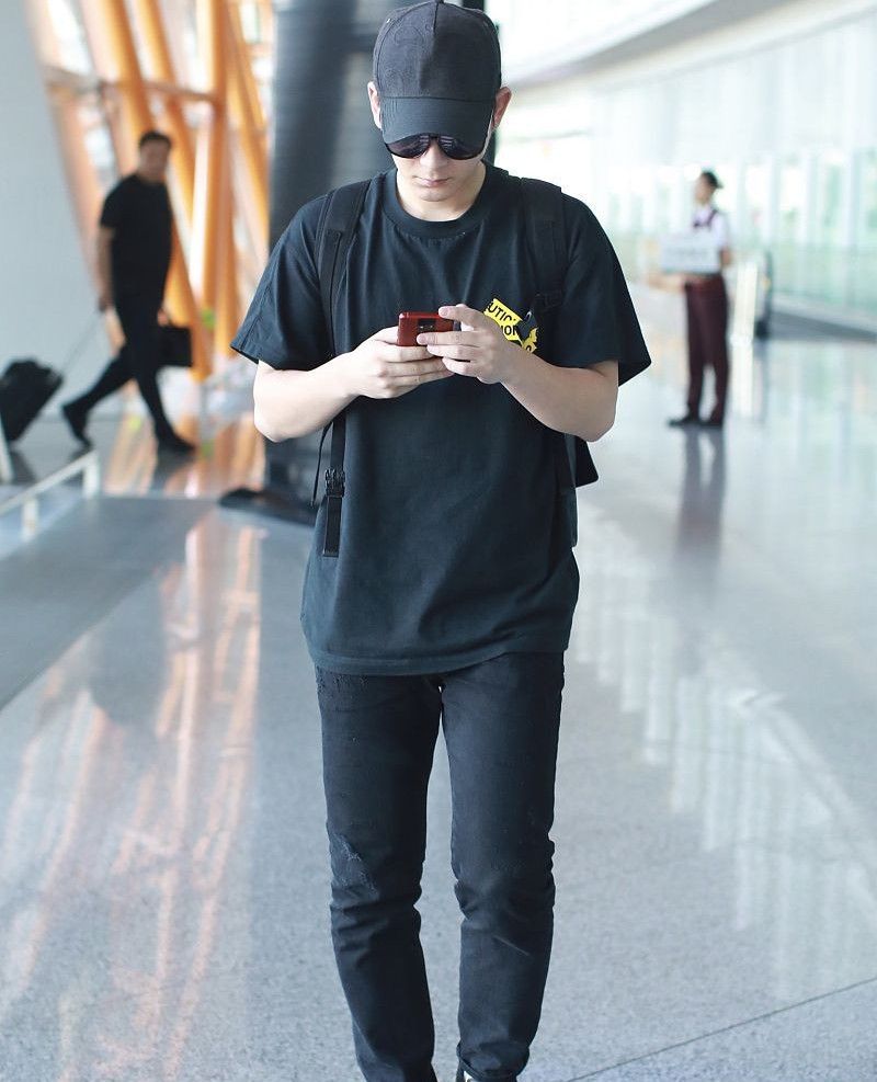 陈翔穿黑色t恤酷劲十足,戴黑色鸭舌帽低头玩手机