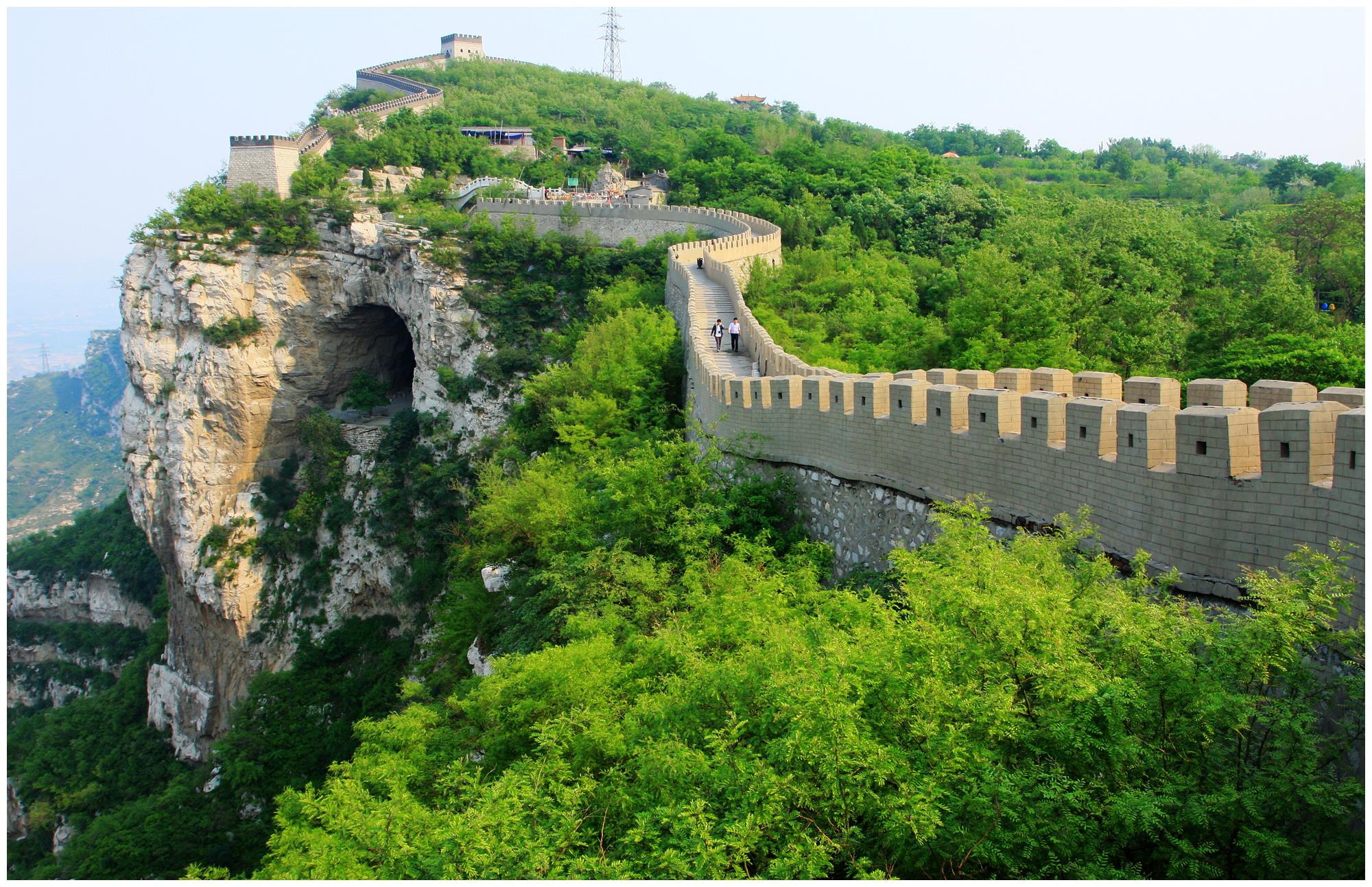 这是中国长城的一部分，蜿蜒于山脉之上，城墙与绿色植被交织，展现出历史与自然的和谐。天空清朗，景色宜人。