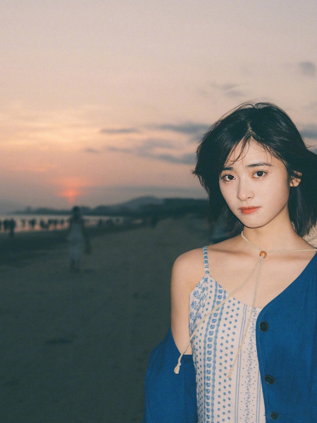 沈月身穿天蓝色印花吊带裙搭配深蓝色外套,海边拍照悠