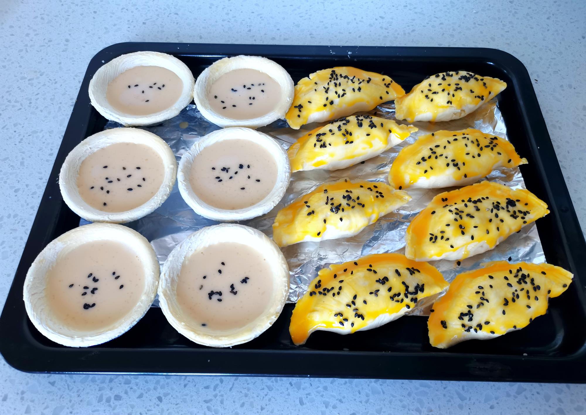 一盘撒了黑芝麻,另一盘没撒,包好的牛角酥刷上一层蛋黄液,然后也撒上