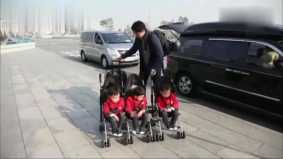 三胞胎整整齐齐坐在婴儿车里,爸爸拖着超大行李箱