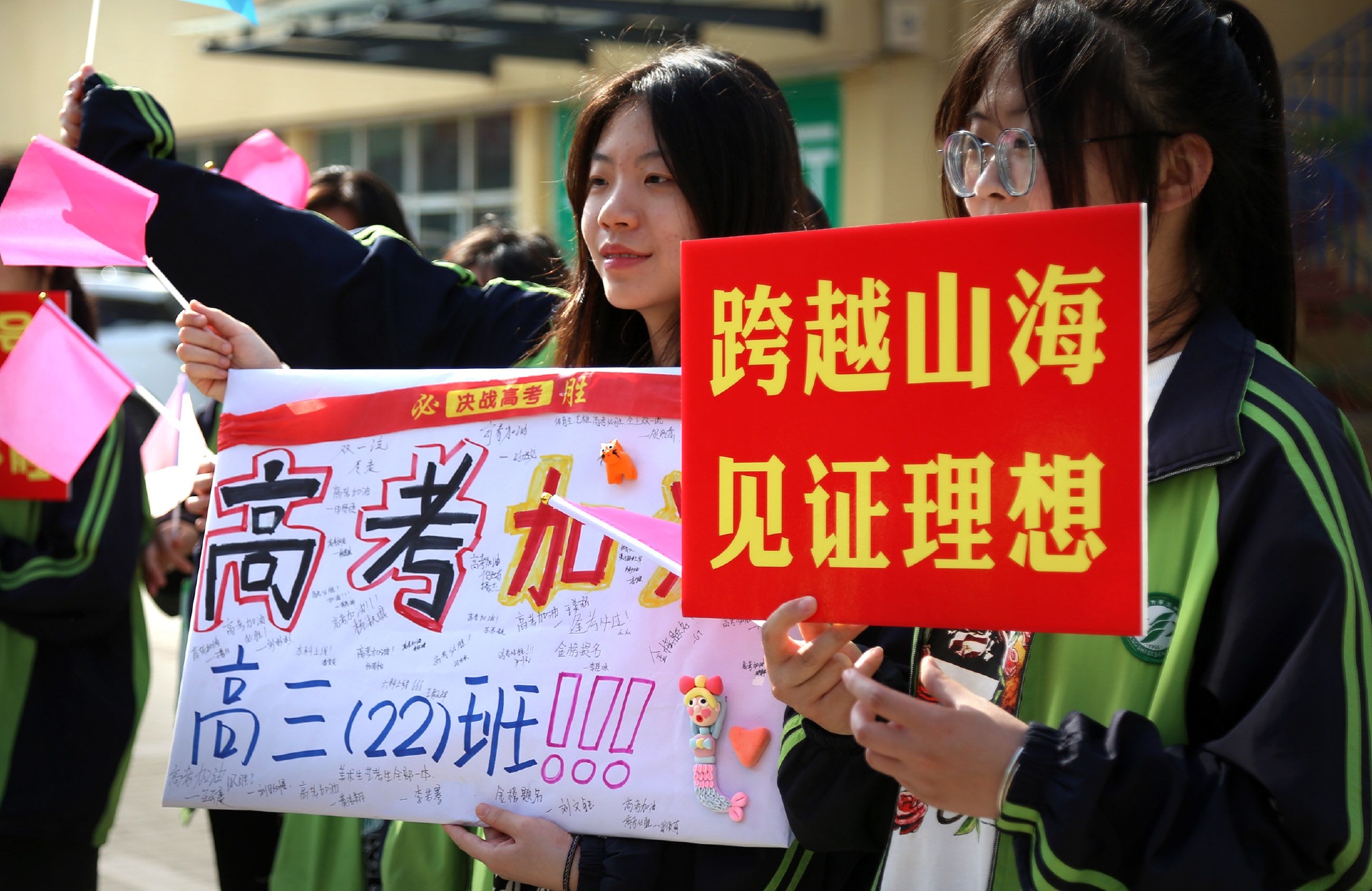 男老师身穿红衣服手拿向日葵为考生加油寓意状元郎一举夺魁