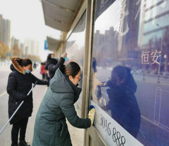 水盆,抹布等清洁工具来到了马路对面的公交站牌进行打扫和清理工作