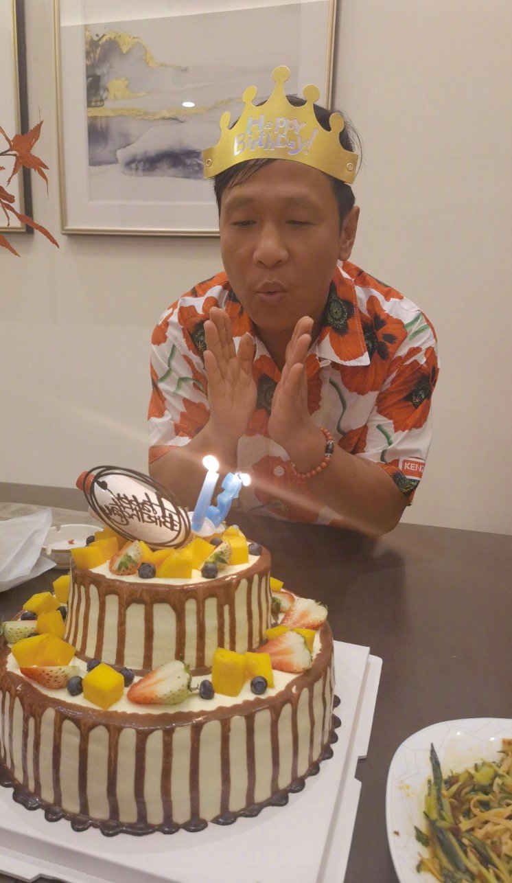 照片中,宋小宝头戴生日皇冠,身穿花纹短袖,双手放在嘴巴前方形成"气道