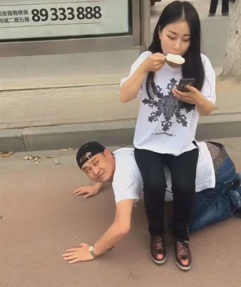 公交站没有座位,男子怕女友累着,竟然跪趴在地让女友坐他身上!