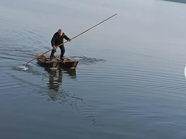 这时一位老人曲着双腿,半蹲着身子站在两条小船上,时而用船篙撑船让其