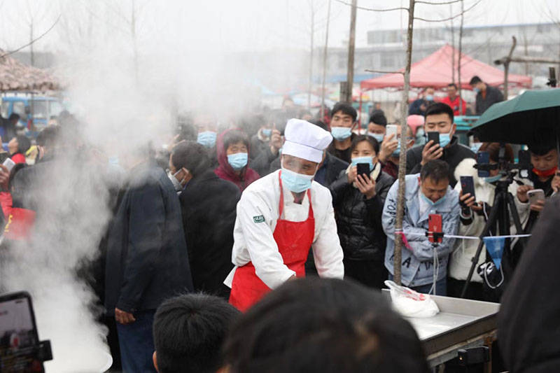 简陋的集市地摊上,程运付现场和面做拉面,案板前后围得里三层外三层