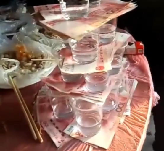 每一个塑料杯底下都放了一摞百元大钞,规则很简单,喝掉里面的酒,就