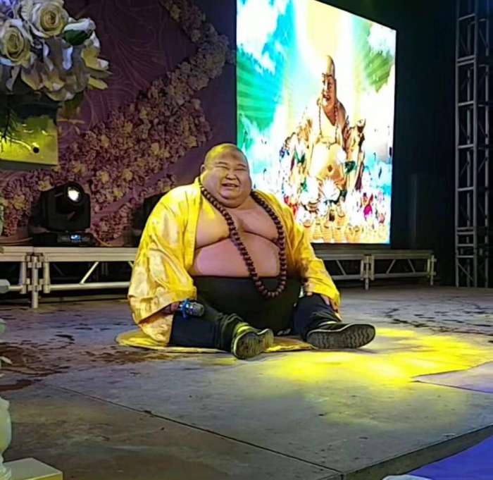 真人版"弥勒佛",表演坐着笑,观众看到后,纷纷朝其扔钱讨吉利