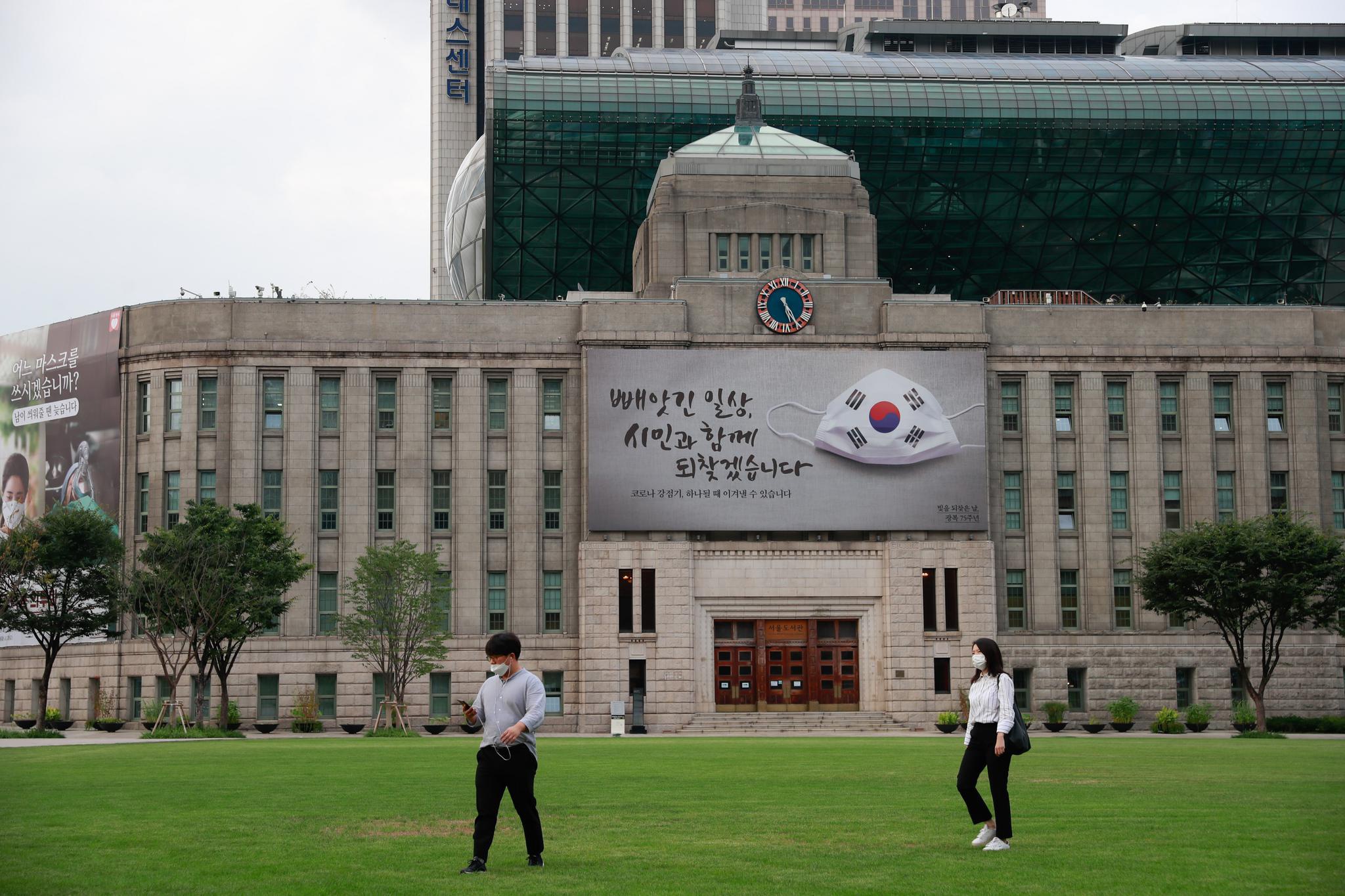 9月15日,戴口罩的行人从韩国首尔市图书馆前的草地上走过.