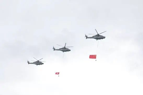 政府飞行服务队直升机在维港上空飞过，展示大型国旗和区旗。图源：港媒