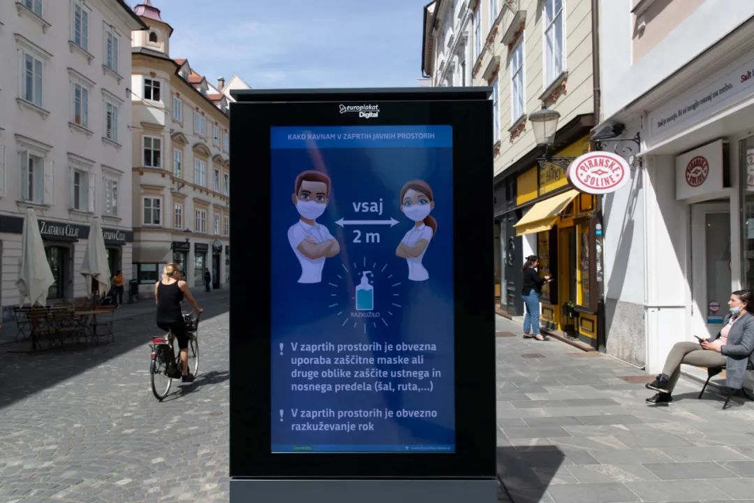 ▲资料图片：在斯洛文尼亚首都卢布尔雅那，一名行人骑车路过提醒人们保持距离的告示牌。新华社发