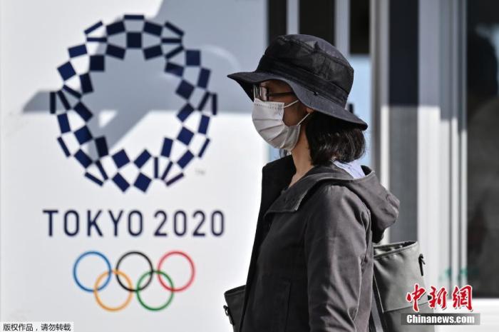 资料图：疫情下的日本。图为当地民众佩戴口罩走过东京奥运会的标识牌。