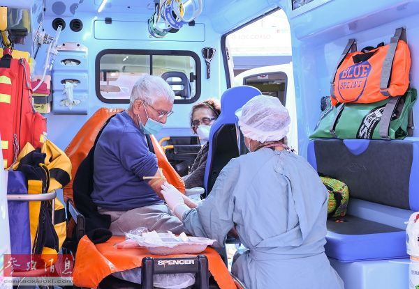 资料图片：两名意大利新冠患者在救护车内接受护士的检查。