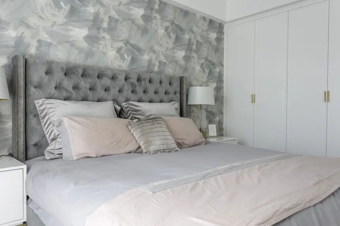 床头墙上贴着灰色涂鸦抽象的墙布,布置银灰色布艺靠背床,带来的夸间