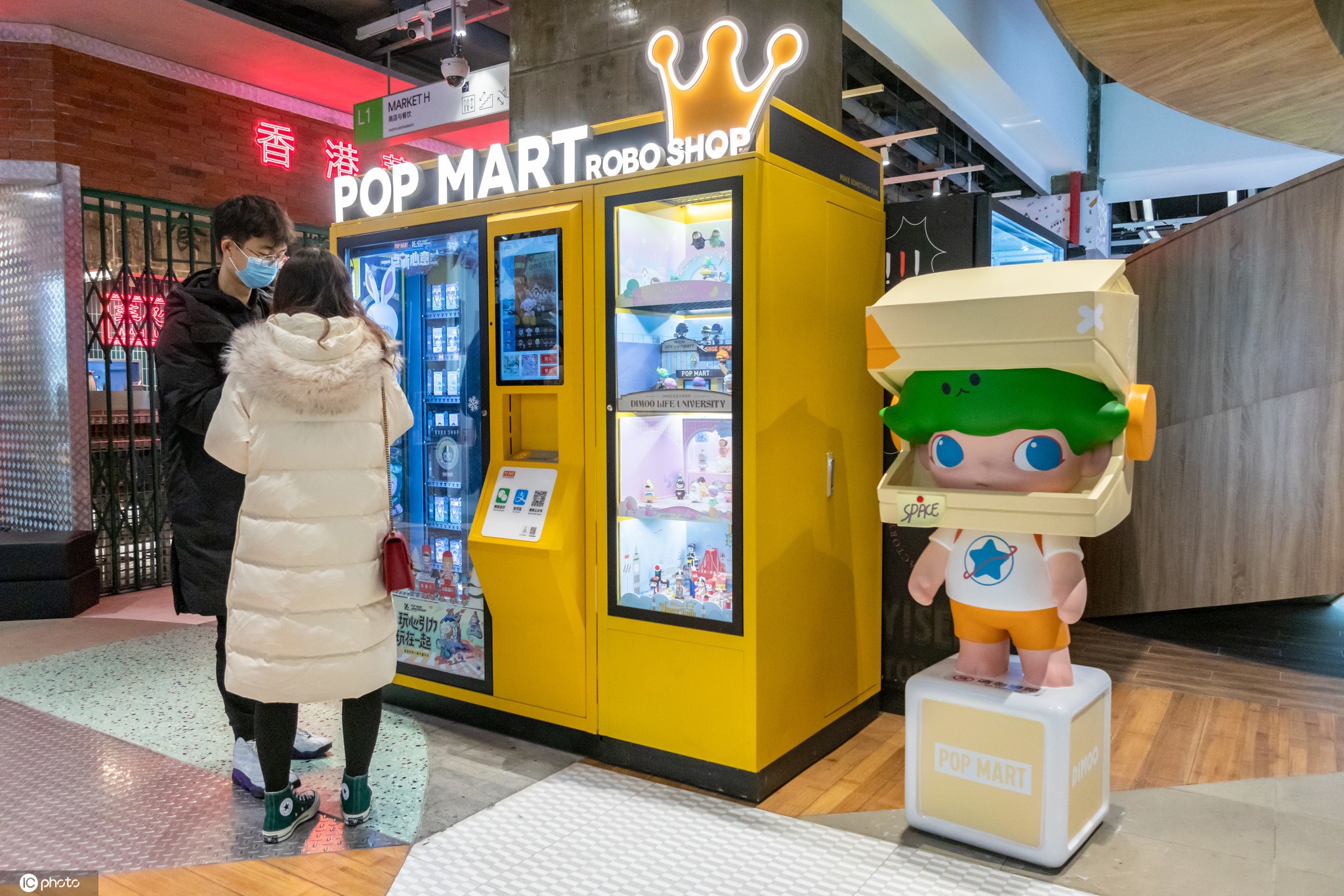 的商场内,一对情侣在一台popmart泡泡玛特售货机前查看刚购买的盲盒