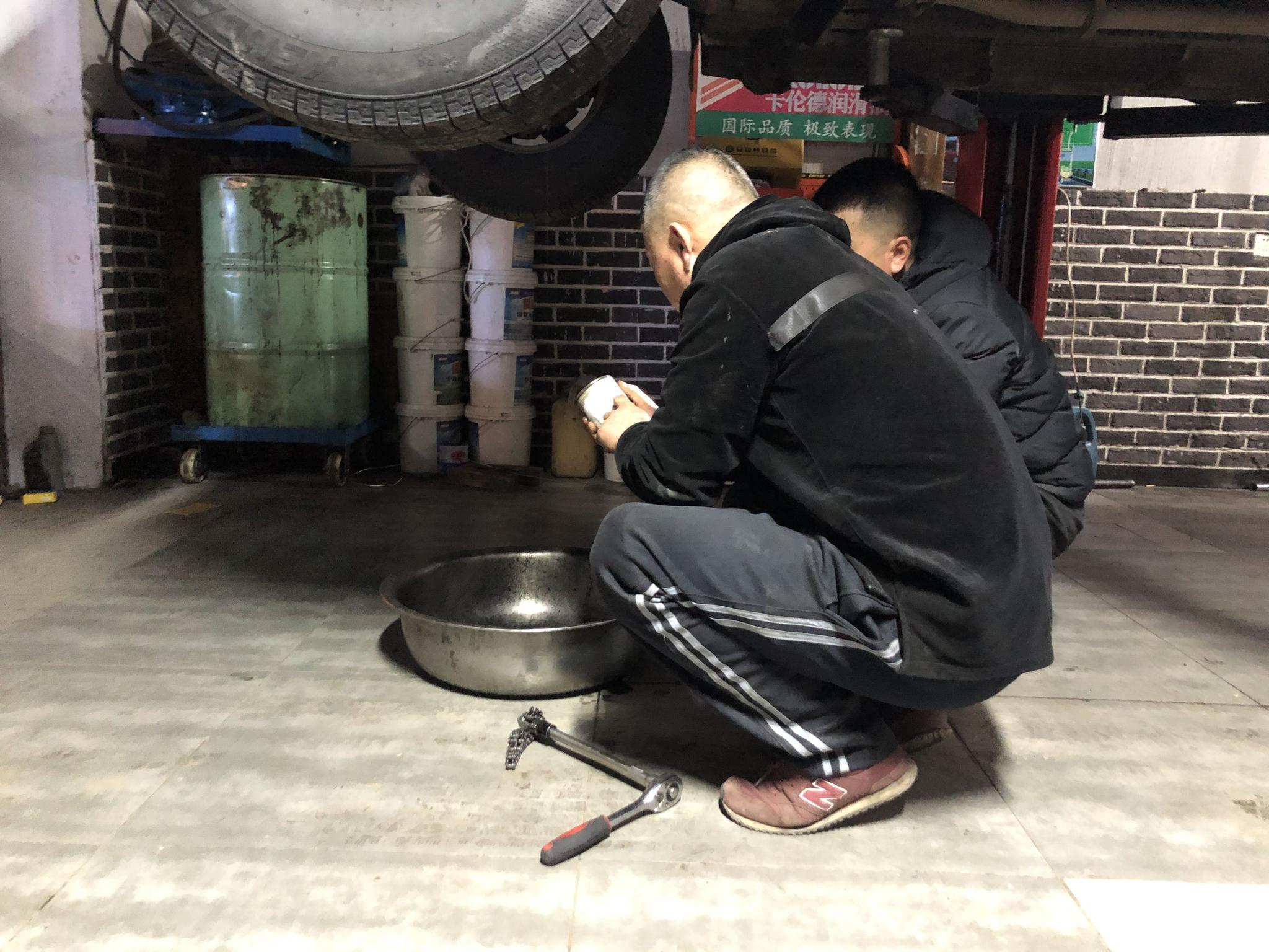 张建国（左一）在自家汽修店内修车。 新京报记者 杜寒三 摄