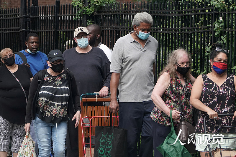 美国纽约曼哈顿区，人们戴着口罩前往食品银行排队领取食物。图自人民视觉