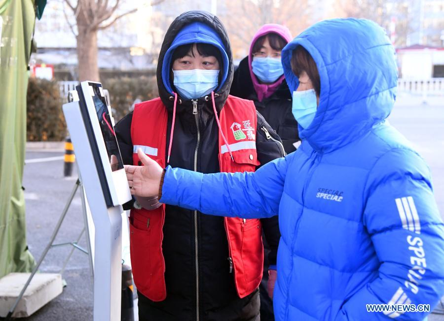 A community worker (L) guides a resident through body temperature check procedure at the entrance of the Hongcheng Huayuan residential compound on Wangquan Street, Shunyi District, Beijing, capital of China, on Dec. 29, 2020. Beijing reported seven new locally-transmitted confirmed COVID-19 cases on Monday, according to the Beijing municipal health commission. The seven patients, who live in the Shunyi District, are all close contacts of earlier reported cases. (Xinhua/Ren Chao)
