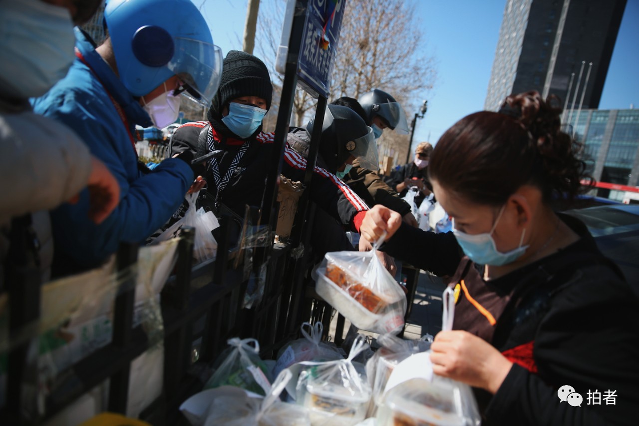 　　△ 3月13日中午，上地十街，外卖员们在一栋汇聚众多餐饮店的商业大楼围栏外领取店家送出来的订单，该商业大楼暂不对外开放。