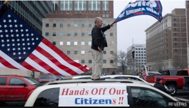 一位手持“让美国再次伟大”条幅的示威者抗议“封城”，图源：路透社