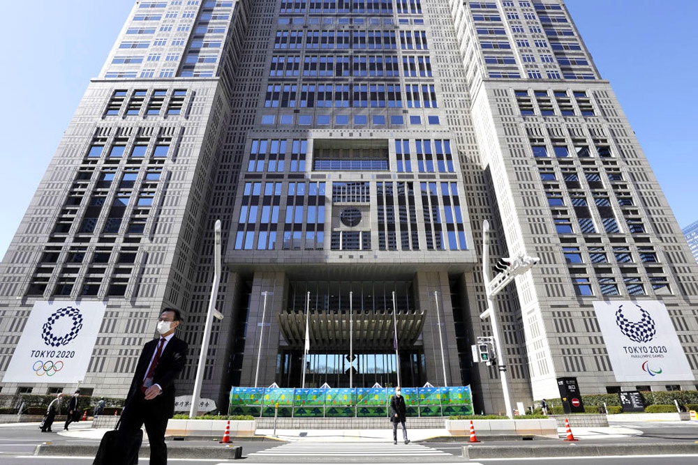 2020年3月11日,日本东京,戴着防护口罩的行人走在东京市政府大楼前,楼