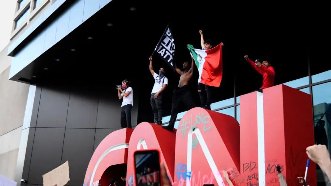  有示威者爬上CNN标志，并挥舞印有“黑人的命也是命”的旗帜。图源：CNN