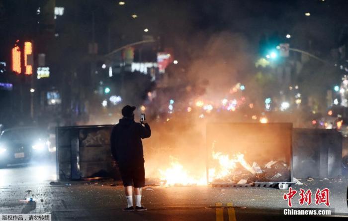 当地时间5月30日，美国洛杉矶抗议活动的中，一名男子在街头燃烧的火堆前自拍。