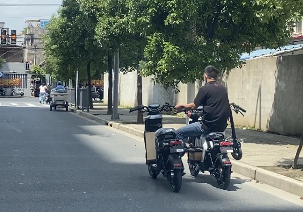 一名男子在杨浦区顺平路上骑电瓶车时,车前横向放了一辆电动滑板车