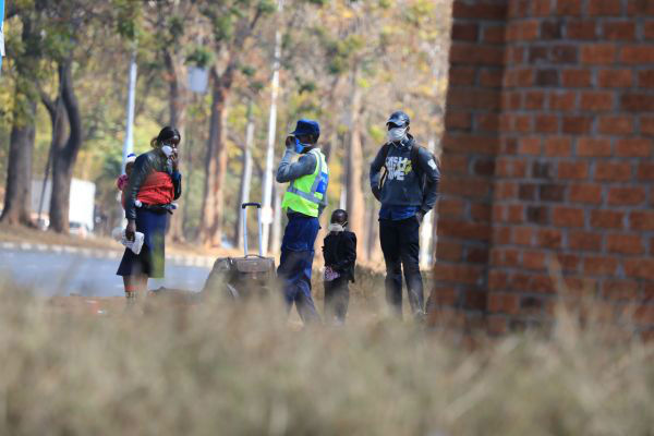  7月22日，在津巴布韦首都哈拉雷，戴口罩的警察和行人交谈。 新华社发