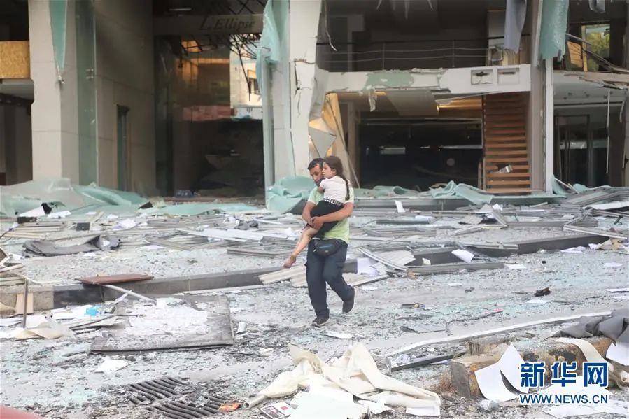 ▲8月4日，在黎巴嫩首都贝鲁特，一名男子抱着孩子走过严重受损的建筑。新华社发（比拉尔·贾维希 摄）