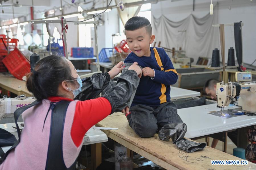 Congcong, the son of Huang Hailong, tries on a protective sleeve his mother made for his grandmother at a garment factory in Shishi, southeast China's Fujian Province, Jan. 26, 2021. Following the resurgence of sporadic COVID-19 cases, many places across China have encouraged residents and migrant workers to stay put to celebrate the Spring Festival, to reduce the flow of personnel and curb the spread of the coronavirus during the holiday period. Huang Hailong, a migrant worker in Shishi, said it would be his first time in past years to spend the holiday in Shishi instead of his hometown in the city of Suining, southwest China's Sichuan Province. Although living with his wife and younger son Congcong, Huang is still missing his parents and elder son who live in the hometown. He made down jackets, protective sleeves, pillows and aprons for them and posted those gifts back home. (Xinhua/Song Weiwei)