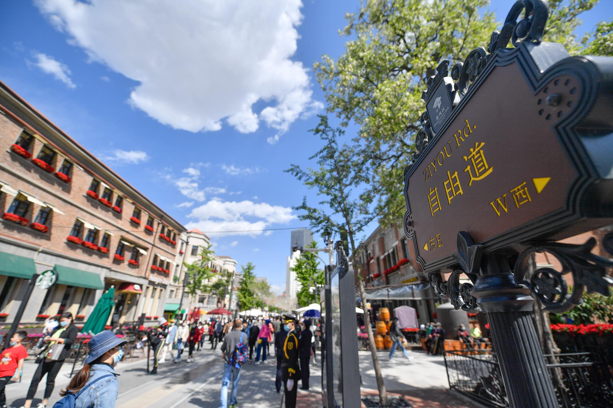 在天津市河北区意式风情街马可波罗广场,游客(中)与巡游演员合影