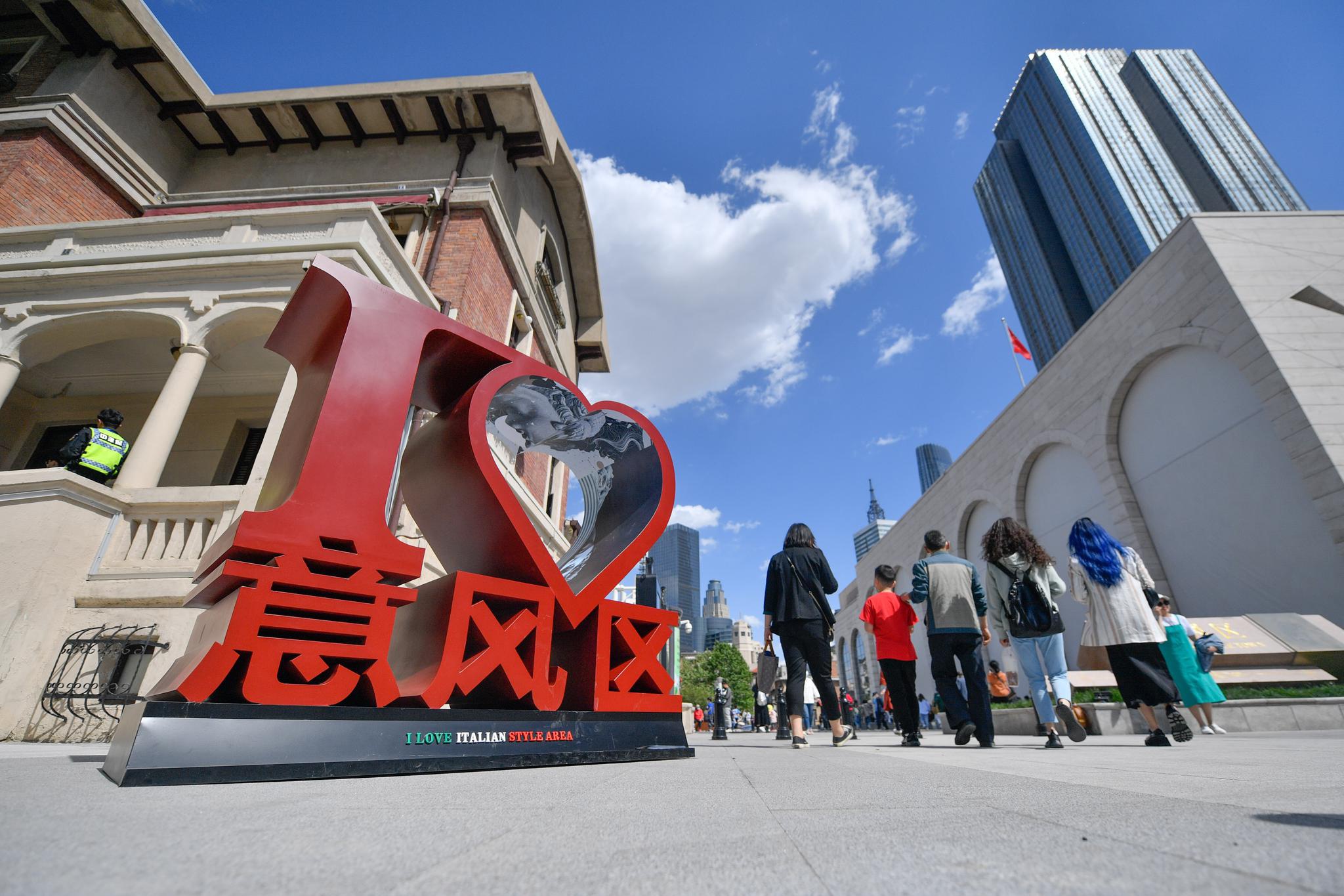 5月1日,在天津市河北区意式风情街马可波罗广场,游客(中)与巡游演员