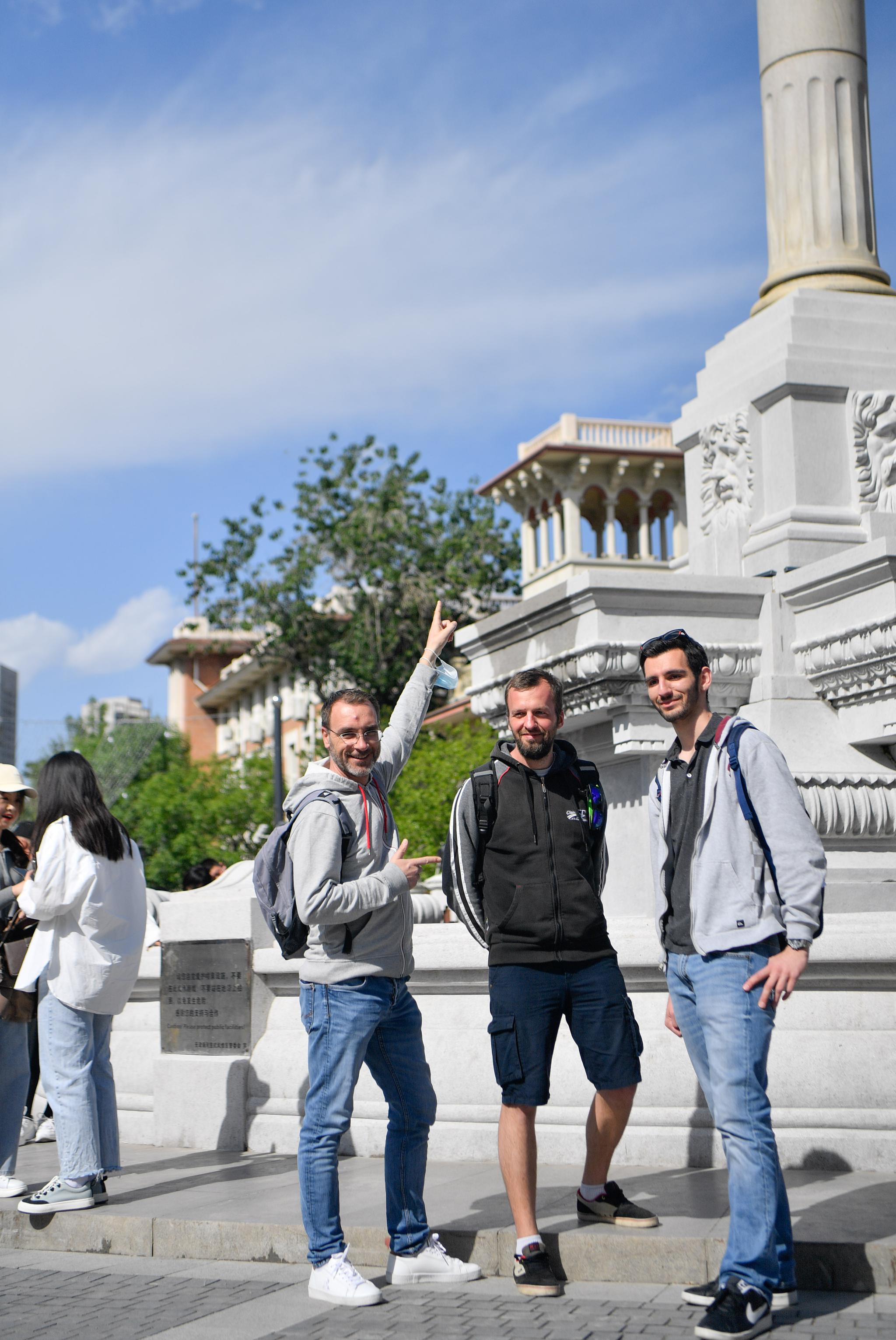 在天津市河北区意式风情街马可波罗广场,游客(中)与巡游演员合影