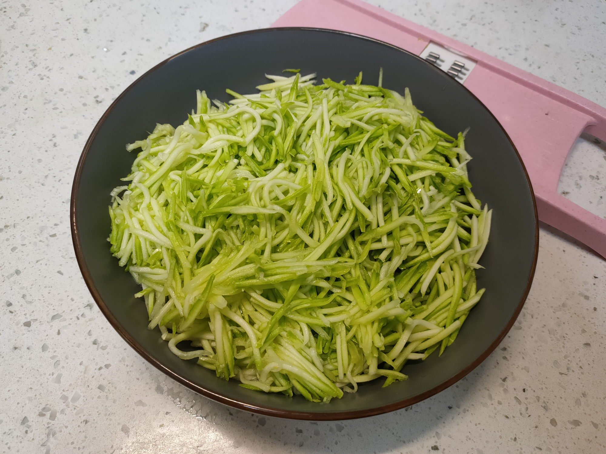 3,把擦好的西葫芦丝放在盆中,加入一茶勺食用盐翻拌均匀,杀出西葫芦中